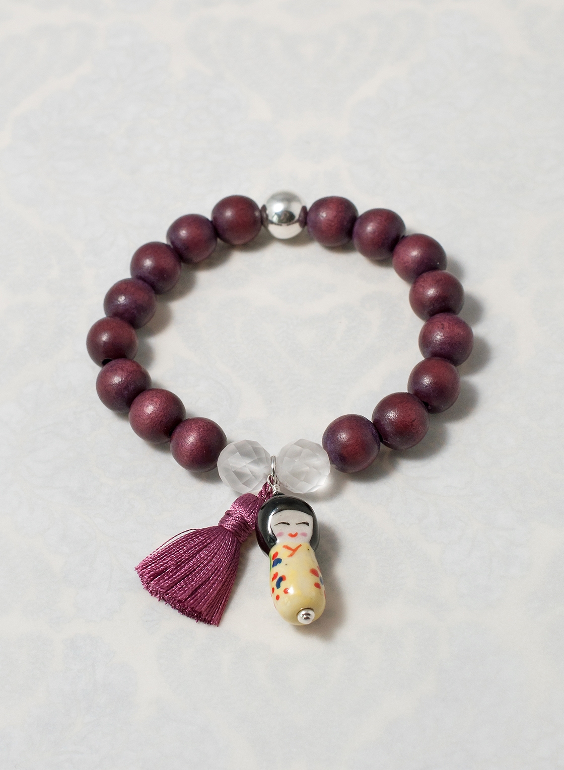 Boho Look Armband mit Holzperlen, zart gelber Kokeshi-Puppe und rosa Quaste.