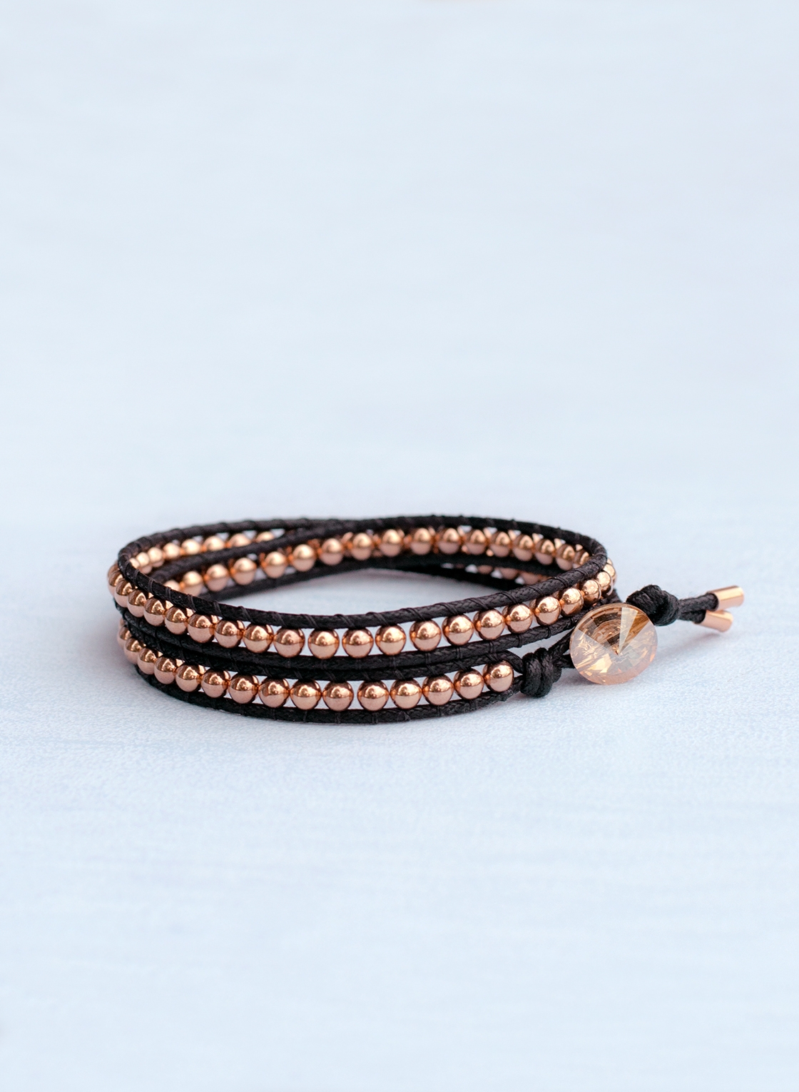 Zweifach gewickeltes Wrap Armband, in rosé goldfarbenem Hämatit und schwarzem Baumwollband, mit Kristallknopf und Endkappen.